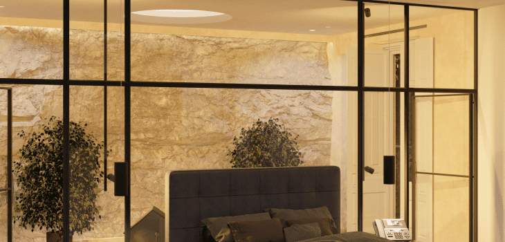 Habitación con banqueta al pie de la cama y jardín interior con roca natural en la Escuela de Diseño de Madrid: un oasis de serenidad y belleza natural.